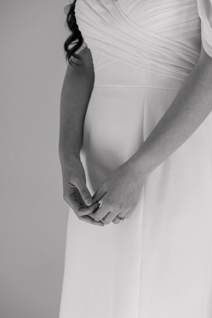 Black-and-white close-up of a bride’s hands resting gently against the draping fabric of her gown, reflecting the quiet detail-focused approach often seen in fine-art wedding photography across Massachusetts.