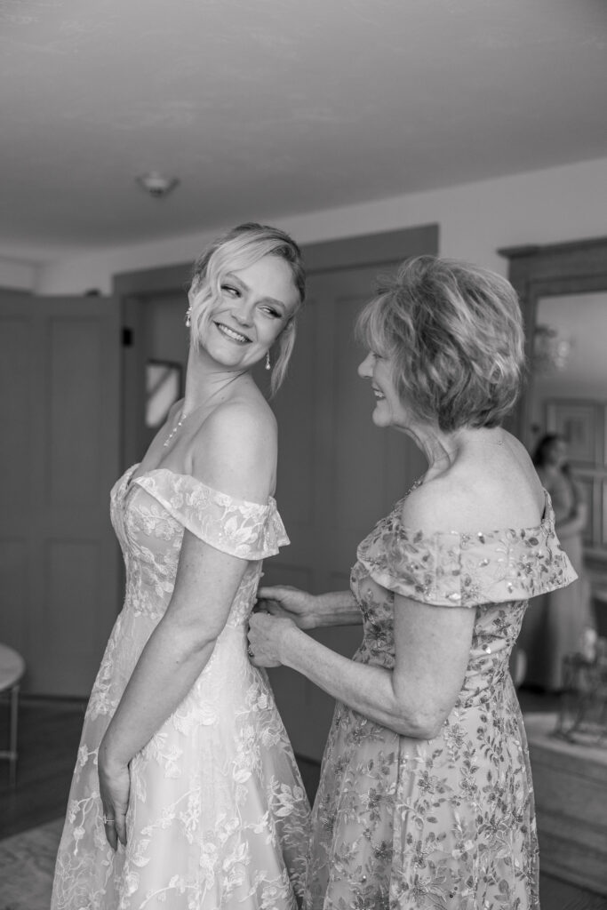 Mother helps button the bride’s gown during a quiet getting-ready moment captured in black and white, showcasing the emotional candid imagery many couples value when choosing Massachusetts wedding photographers.