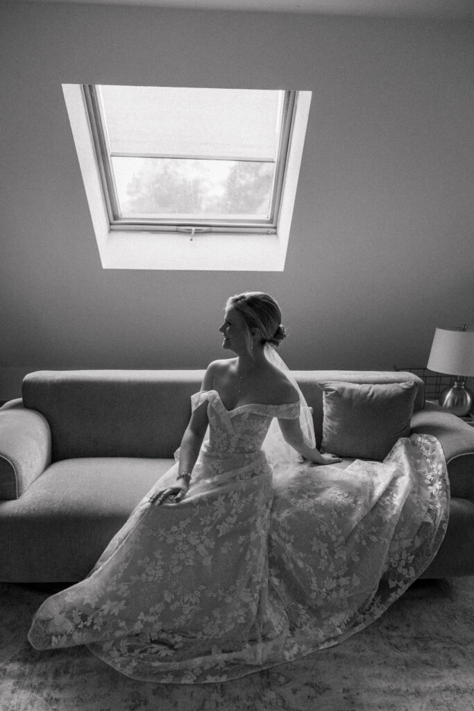Bride sits beneath a skylight in a black-and-white bridal portrait with her gown spread around her, capturing the intimate atmosphere often found at small wedding venues Massachusetts couples love.