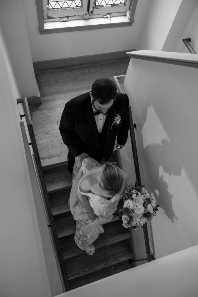 Black-and-white overhead portrait of a bride and groom meeting on a staircase before the ceremony, photographed inside one of the intimate small wedding venues Massachusetts offers.
