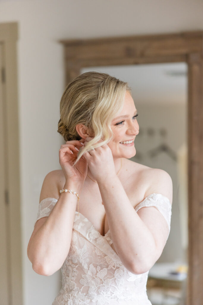 Bride adjusts her earring in soft natural light while getting ready before the ceremony, photographed with the clean and timeless aesthetic associated with luxury wedding photographers in Massachusetts.