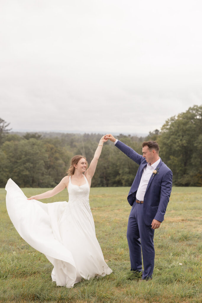 Bride twirls across an open field while holding hands with her groom during a windswept portrait session, showcasing the movement and emotion often captured in artistic Massachusetts wedding photography.
