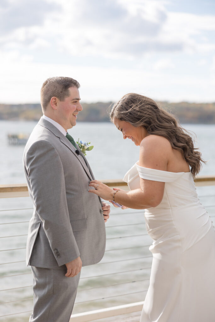 Bride adjusts the groom’s boutonniere while they stand together overlooking the harbor before the ceremony, reflecting the candid and relaxed approach many couples want from Cape Cod wedding photographers.