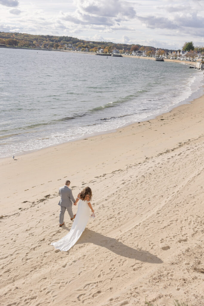 Overhead beach portrait of a newly married couple standing near the water with long shadows stretching across the sand, capturing the coastal scenery often featured in Cape Cod wedding photography.