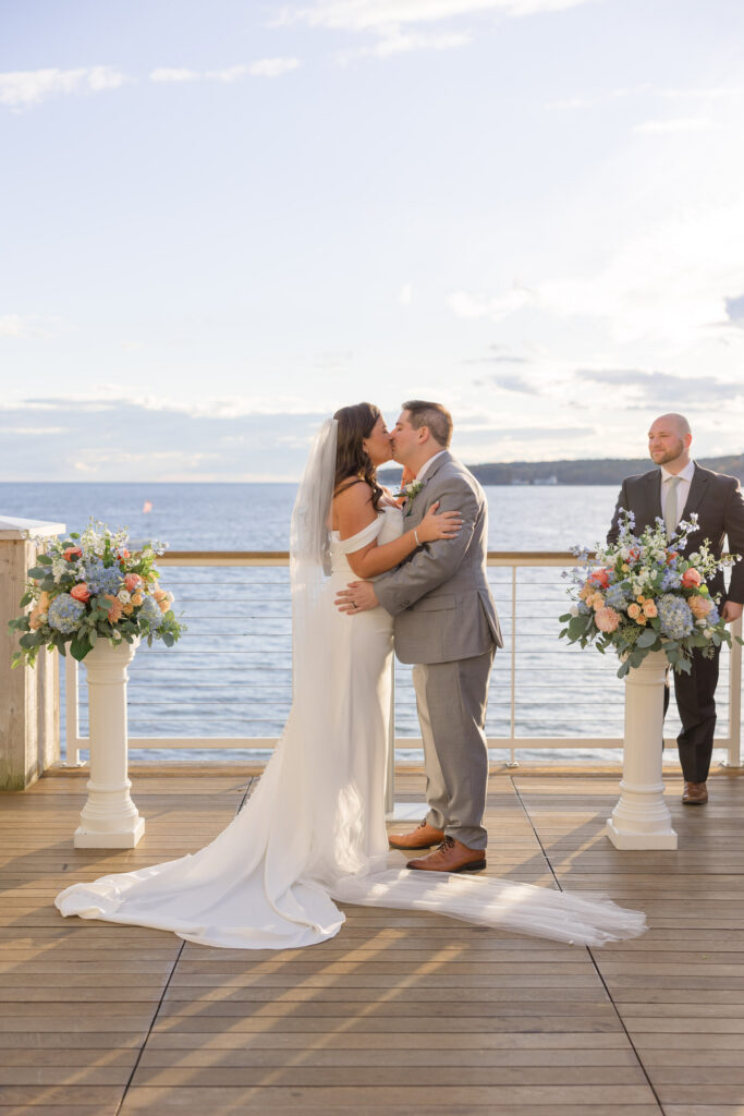 Bride and groom exchange vows on a waterfront ceremony deck surrounded by pastel florals and ocean views, showcasing the elegance of waterfront wedding venues Massachusetts couples often search for.
