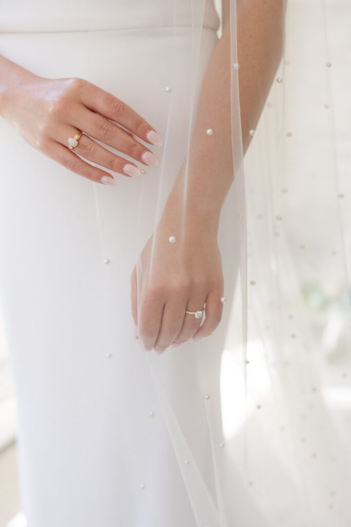 Close-up bridal portrait featuring delicate pearl details, a flowing veil, and wedding rings against a minimalist gown, reflecting the refined editorial style often seen in Cape Cod wedding photography.