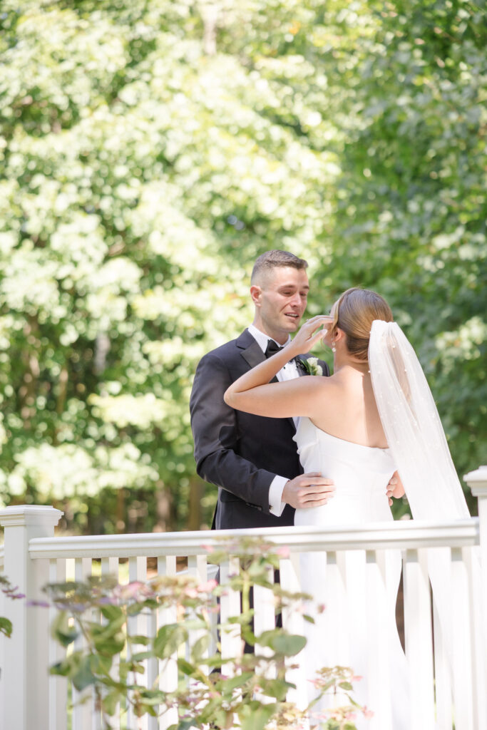Newly married couple embraces on a white porch surrounded by lush greenery during an outdoor portrait session, a natural and romantic moment often prioritized by a Massachusetts wedding photographer.