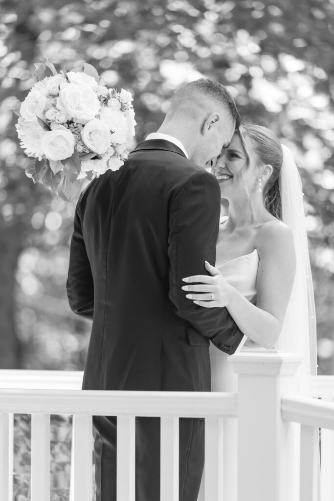 Couple embraces on a white porch during a quiet black-and-white portrait session beneath soft tree light, reflecting the intimate atmosphere often found at small wedding venues Massachusetts couples love.