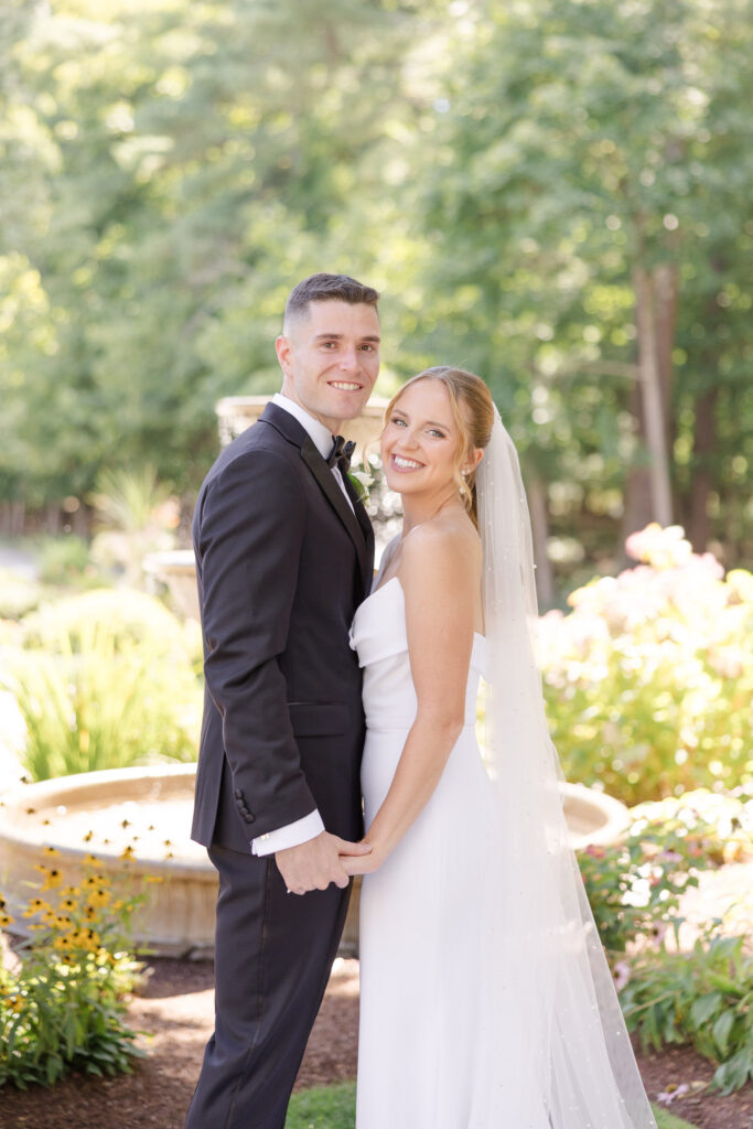Bride and groom pose together in a sunlit garden surrounded by greenery and florals after the ceremony, photographed at one of the romantic garden wedding venues Massachusetts is known for.