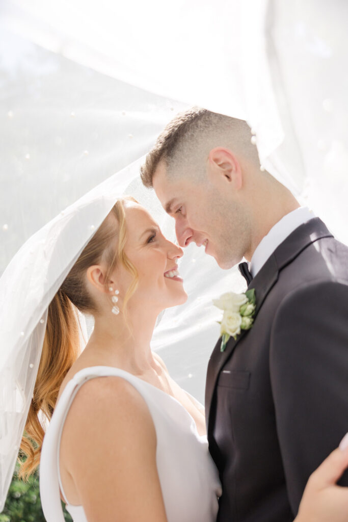 Bride and groom lean forehead to forehead beneath a flowing veil during an intimate close-up portrait, reflecting the light and airy editing style many Massachusetts wedding photographers are known for.