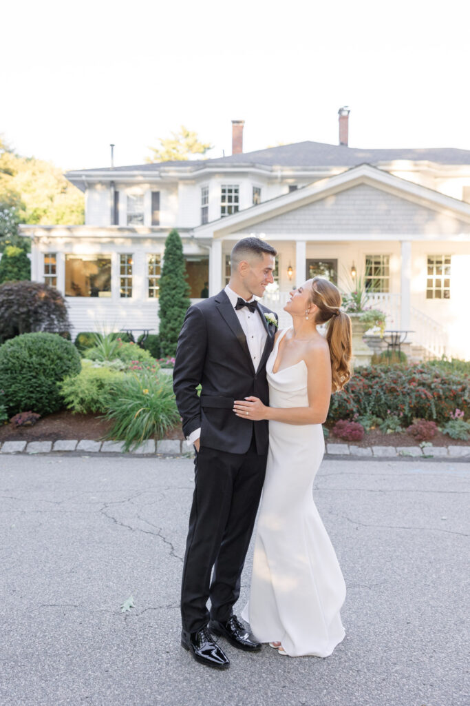 Bride and groom stand together outside a coastal estate venue surrounded by manicured landscaping and soft evening light, reflecting the elegance of top wedding venues in Massachusetts.