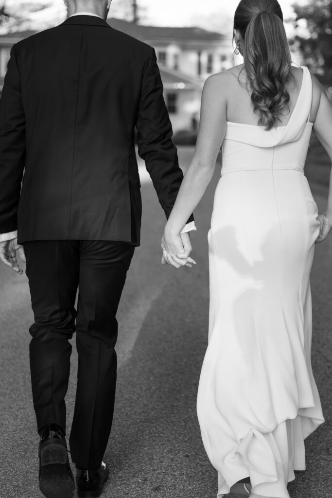 Black-and-white portrait of a newly married couple holding hands while walking away together after the ceremony, photographed at one of the more intimate full-service wedding venues Massachusetts couples often choose.